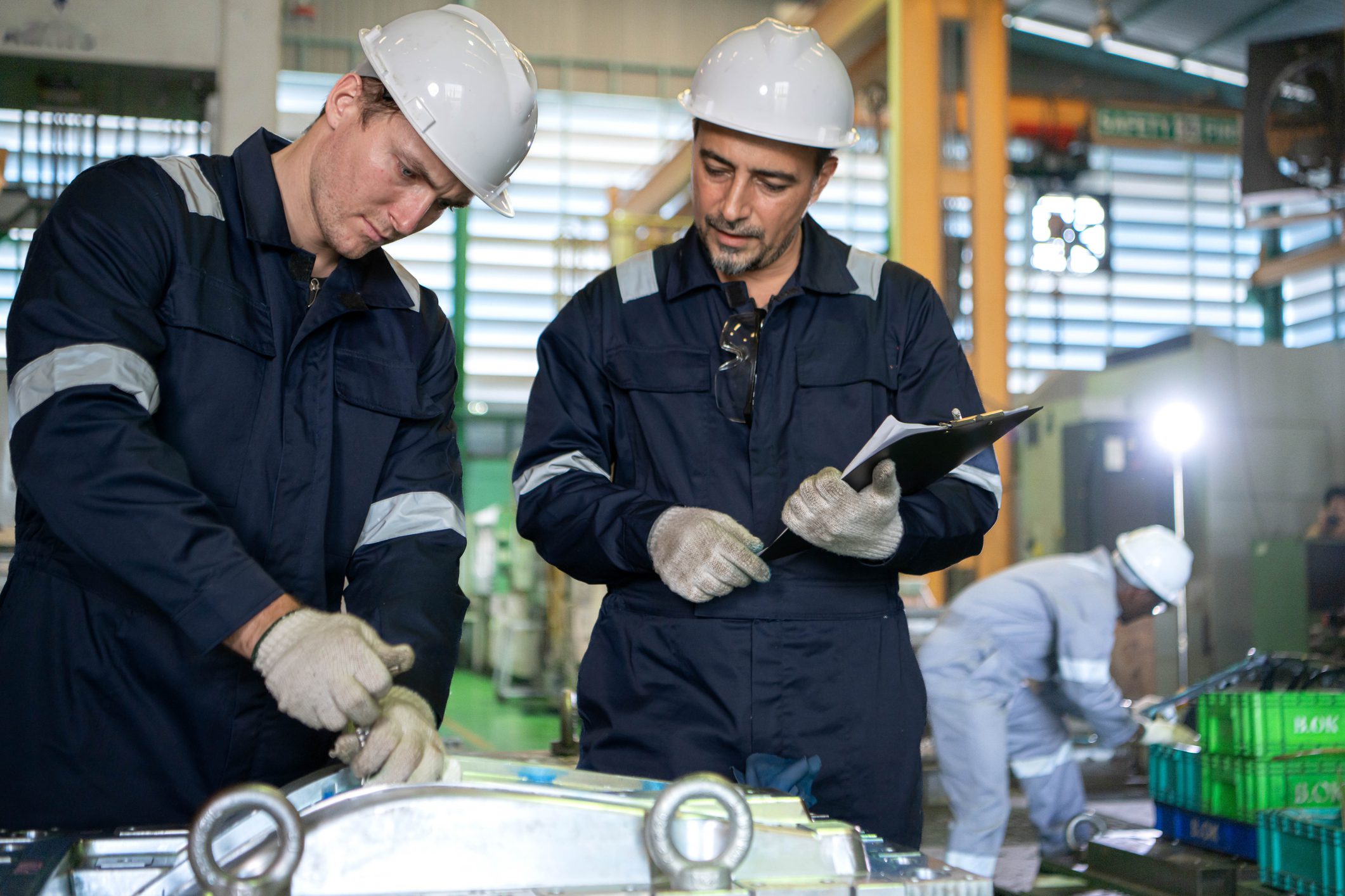 Engineers and factory technicians inspecting industrial machine parts and recording production information inside a manufacturing plant
